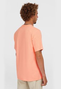 Kortærmet T-shirt med rund hals i lys koral, der har en blød tekstur og subtilt horisontalt mønster, båret med beige bukser.