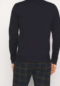 Marinblått stickat tröja med långa ärmar, ribbade manschetter och nederkant. Slät textur, rundad halsdesign, kombinerad med rutiga byxor.