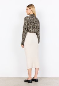 Schwarz-beige gemustertes langärmliges Hemd, kombiniert mit einem cremefarbenen, gerippten Midirock und schwarzen Ballerinas, das eine taillierte Silhouette präsentiert.