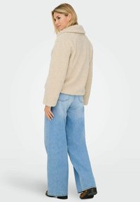 Beige, fluffy jacket with a wide collar and long sleeves, paired with light blue wide-leg jeans and brown ankle boots.