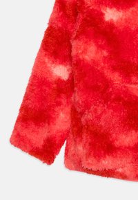 Rød, fluffy jakke med et tekstureret, fnugget materiale; har et tie-dye mønster i varierede nuancer af rød og pink. Lange ærmer er synlige.