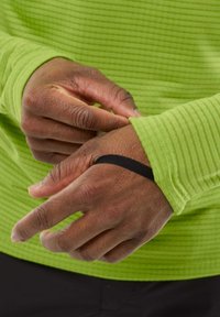 Chemise verte à manches longues avec une texture à côtes horizontales ; bracelet élastique noir au niveau du poignet ; mains ajustant la manche.