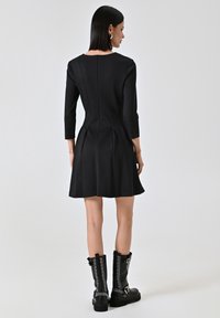 Schwarzes Kleid mit langen Ärmeln und ausgestellt Rock, mit einem Reißverschluss im Rücken. Kombiniert mit kniehohen schwarzen Stiefeln mit Nieten.