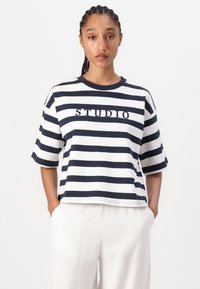 Stribet t-shirt i marineblå og hvid, med rund halsudskæring og korte ærmer. Har broderet "STUDIO" tekst på forsiden. Fremstillet af bomuldsstof.