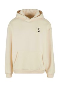 Kremfarget hettegenser laget av mykt stoff, med en frontlomme, ribbestrikkede mansjetter, og en liten svart spade og bokstaven "K" logo på brystet.