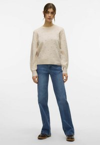 Maglione beige lavorato a maglia con bobble testurizzati, scollatura a girocollo e maniche lunghe abbinato a jeans svasati blu e stivali alla caviglia marroni.