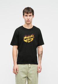 Μαύρο βαμβακερό t-shirt με γραφικά φλόγας και τη φράση "WU-TANG CLAN" σε κίτρινο και κόκκινο. Είχε κοντά μανίκια και χαλαρή εφαρμογή.