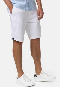 Pantaloni corti bianchi in cotone con risvolti, dotati di tasche laterali e dettagli neri vicino all'orlo. Accoppiati con sneakers bianche.