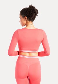 Top sportivo a maniche lunghe, corto, di colore corallo acceso con accenti a strisce bianche all'orlo. Texture liscia e design aderente.