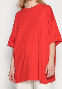 T-shirt rossa oversize in cotone morbido, con maniche corte, colletto tondo e vestibilità ampia. Texture liscia con un aspetto informale.