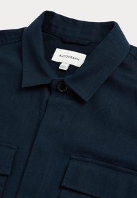 Camisa azul marino de tejido texturizado, con cierre de botones y dos bolsillos en el pecho. Presenta un cuello con puntas y la etiqueta "AUTOGRAPH".