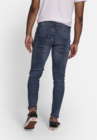 Tunna blå denimjeans med en urtvättad finish, fem fickor och sömnadsdetaljer. Bärs med svarta skate-skor som visar ankeldetaljer.