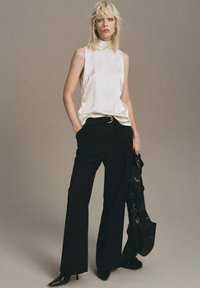 White sleeveless top with high neckline, paired with black wide-leg trousers. Black accessories include a handbag. Textured, sleek materials.