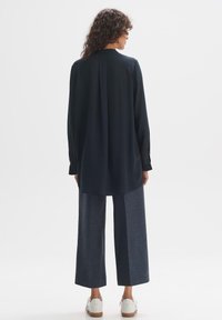 Marineblauses, langärmlig mit gefaltetem Rücken, kombiniert mit weiten grauen Hosen und weißen Sneakers, mit einer glatten Textur und geradem Schnitt.