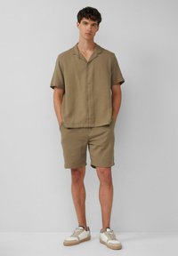 Khaki korte mouwen overhemd met een relaxte pasvorm, gecombineerd met bijpassende shorts. Kenmerken zijn de gestructureerde stof en witte sneakers.