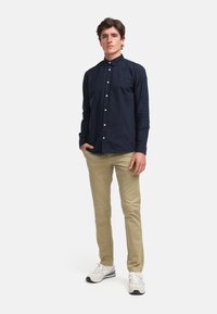 Chemise bleu marine à manches longues, assortie à un pantalon chino beige et des baskets blanches. La chemise présente un col et des détails de poche avant.