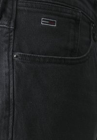 Los vaqueros de mezclilla negros presentan un diseño clásico de cinco bolsillos con un pequeño parche de logo y herrajes metálicos cerca del bolsillo. Tejido texturizado.