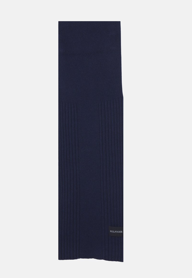 Sciarpa lavorata a maglia blu navy con texture a coste, con un'etichetta con logo nella parte inferiore. Il design è lungo e di forma rettangolare.