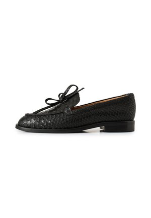 Mocasín de cuero negro texturizado con tacón bajo y un detalle de lazo atado en la parte superior, mostrado de lado.
