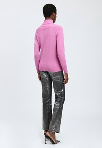 Rosa, figurbetontes Sweatshirt mit hohem Kragen und gerippten Bündchen. Kombiniert mit glänzenden, metallisch silbernen Hosen mit Seitennähten.