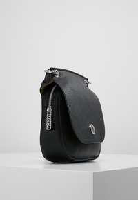 Black leather handbag with a textured finish, a front flap, silver hardware, and a side zipper detail. Compact, with rounded edges.