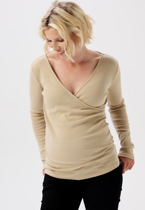 Beige lange mouwen wikkeltop gemaakt van ribstof met een v-hals en een getailleerd ontwerp. Gecombineerd met zwarte broek, die de taille accentueert.