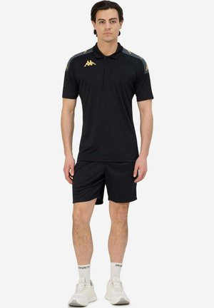 Polo shirt de sport noir à manches courtes, avec des accents de logo doré et des rayures grises sur les épaules, associé à un short noir assorti.