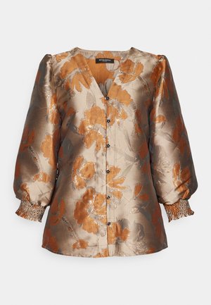 Blouse à manches longues en satin, présentant un motif floral en or et orange. Design en V, fermeture par boutons et manches froncées avec un détail de smocks.