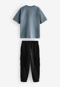 Hellblaues Baumwollhemd mit kurzen Ärmeln, kombiniert mit schwarzen Baumwoll-Cargohosen mit Seitentaschen und elastischen Bündchen.
