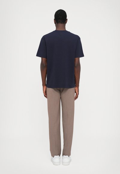 T-shirt en coton bleu marine avec un col rond, coupe décontractée et manches courtes, associé à un pantalon beige ajusté et des baskets blanches.