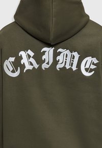 Parte trasera de una sudadera con capucha de color verde oscuro con grandes letras blancas bordadas al estilo gótico que dicen "CRIME" a lo largo de los hombros.