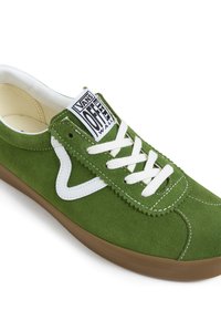 Baskets en daim vert avec lacets blancs, présentant un patch logo blanc et un accent ondulé sur le côté. Semelle en caoutchouc brun, doublure intérieure lisse.