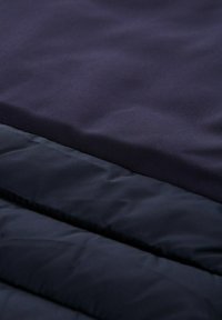 Granatowy materiał tekstylny z gładką, matową powierzchnią oraz pikowanym, wyściełanym fragmentem o lekko błyszczącym wykończeniu, ukazującym gradient kolorów.