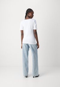 White short-sleeve t-shirt in lightweight fabric, paired with light blue wide-leg jeans. Features a simple round neckline and relaxed fit.