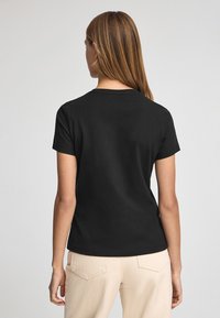 Svart kortärmad t-shirt med rund halsringning, slät yta och enkel design, kombinerad med ljusa byxor.