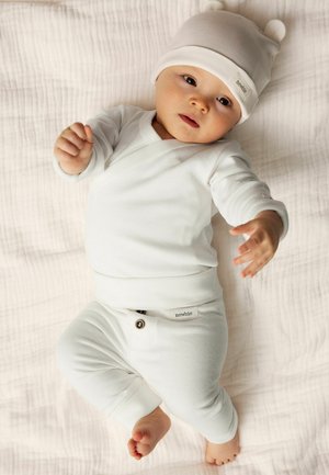 Ensemble de haut à manches longues et de pantalon blanc pour nourrissons, fabriqué dans un tissu doux, avec un détail de bouton et un bonnet assorti avec des oreilles d'ours. Fond plat et texturé.