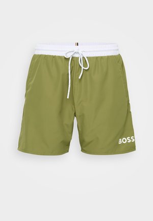 Shorts de baie verde oliv cu un elastic alb la talie, șnur ajustabil și logo-ul "BOSS" imprimat în alb pe piciorul stâng.