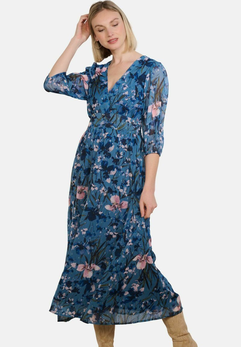 Vestido maxi de tela azul translúcida con patrones florales en rosa y blanco, escote en V, mangas tres cuartos y cintura ceñida.