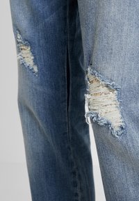 Ljusblå denimjeans med slitna lappar, fransade kanter och synlig sömdetalj. Raka ben med en använd look.