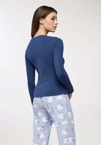 Niebieska bluzka z długim rękawem o dopasowanym kroju, zestawiona z jasnoniebieskimi spodniami od piżamy z białymi wzorami owiec i chmur.