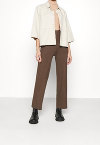 Beige oversized skjortjacka med två framfickor, kombinerad med bruna ribbade vida byxor och svarta ankelstövlar.