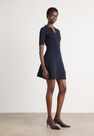 Navy short-sleeve dress with a collar, fitted bodice, and flared skirt. Worn with black pointed-toe heels. Smooth texture.