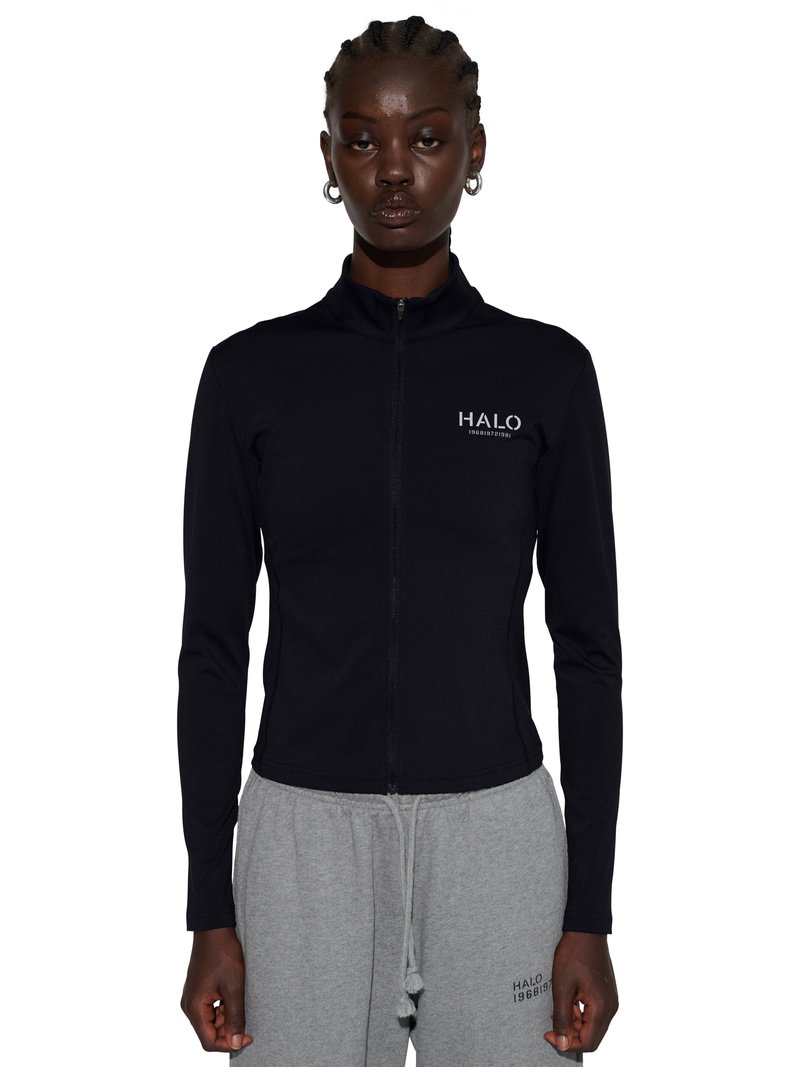 Czarna kurtka na zamek z logo "HALO" noszona przez stojącą osobę w szarych dresach z małym logo na lewym udzie.