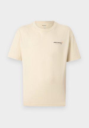 Beigen värinen lyhythihainen t-paita, jossa on pieni McLaren Formula 1 -tiimin logo vasemmassa rinnassa ja pyöreä pääntie.