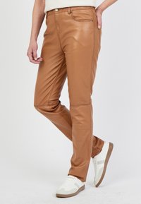 Tan neplederen broek met een getailleerd ontwerp, voorzakken en een subtiele glans, gecombineerd met witte sneakers met lichtbruine accenten.