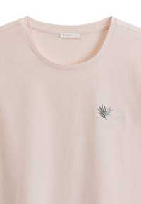 Jasnoróżowa bawełniana koszulka z okrągłym dekoltem, ozdobiona małym haftowanym wzorem liścia z napisem "ATLANTIC" pod spodem.