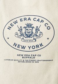 Canvas stof met blauw patroon met het logo van "New Era Cap Co", "Buffalo" en "New York." De tekst bevat het oprichtingsjaar, 1920.