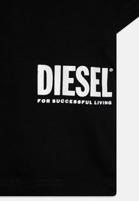 Črna bombažna majica z bold belim napisom "DIESEL" in "ZA USPEŠNO ŽIVLJENJE" na sprednji strani. Gladka tekstura s klasičnim dizajnom okroglega izreza.