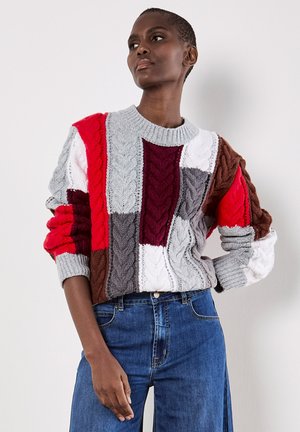 Pull en tricot coloré avec un design en patchwork dans des teintes de gris, rouge, blanc, marron et violet. Comprend des motifs de tricot torsadé et des poignets côtelés.