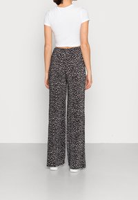 Pantalon large à fleurs noires avec un motif blanc, tissu léger, taille élastique, associé à un haut blanc à manches courtes.